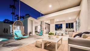 Un espace de vie extérieur moderne, doté de fauteuils suspendus, d’une piscine et d’un coin repas.