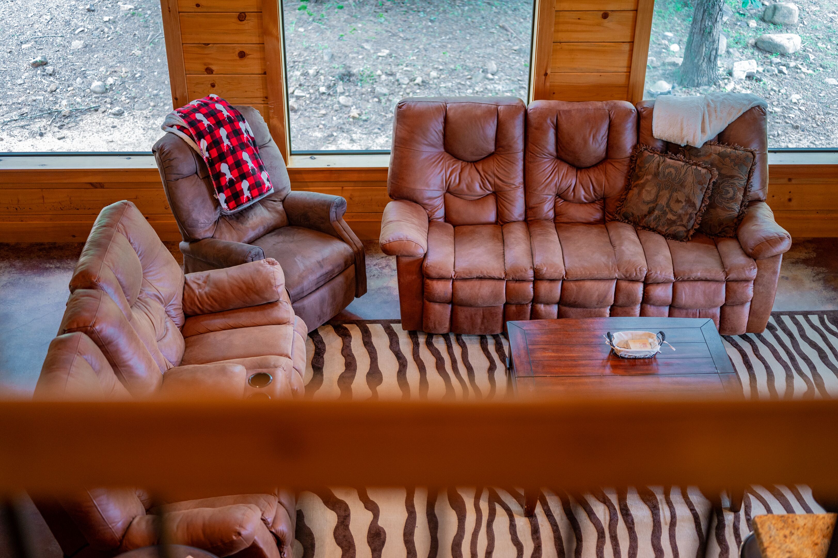 Une pièce chaleureuse avec une grande fenêtre, deux fauteuils en cuir, un tapis à motifs zébrés et une petite table en bois sur laquelle se trouve un bol.
