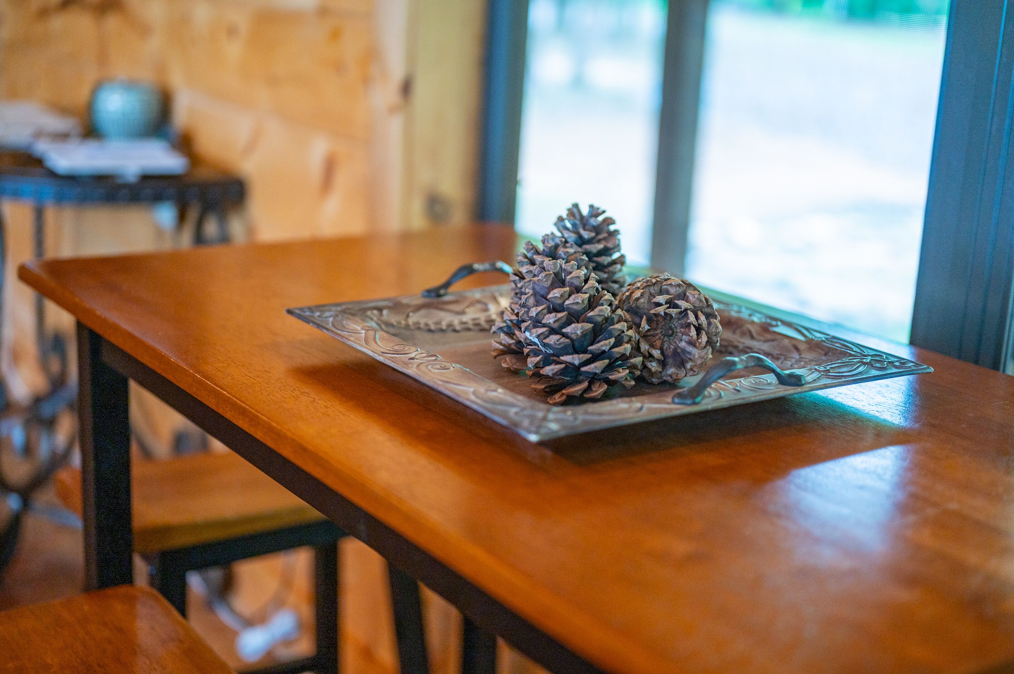 A wooden table with a decorative tray holding pine cones.
