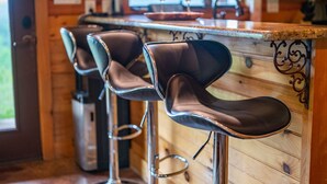A bar area with wooden walls, metal bar stools, and a countertop with two wine glasses. - Mountain Vista Retreat-Issi is secluded, with sunset views of the Kiamichi Mnts. (Smithville)