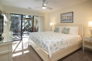 A bedroom with a bed, a ceiling fan, a nightstand, a lamp, a framed picture on the wall, and a sliding glass door leading to a balcony.