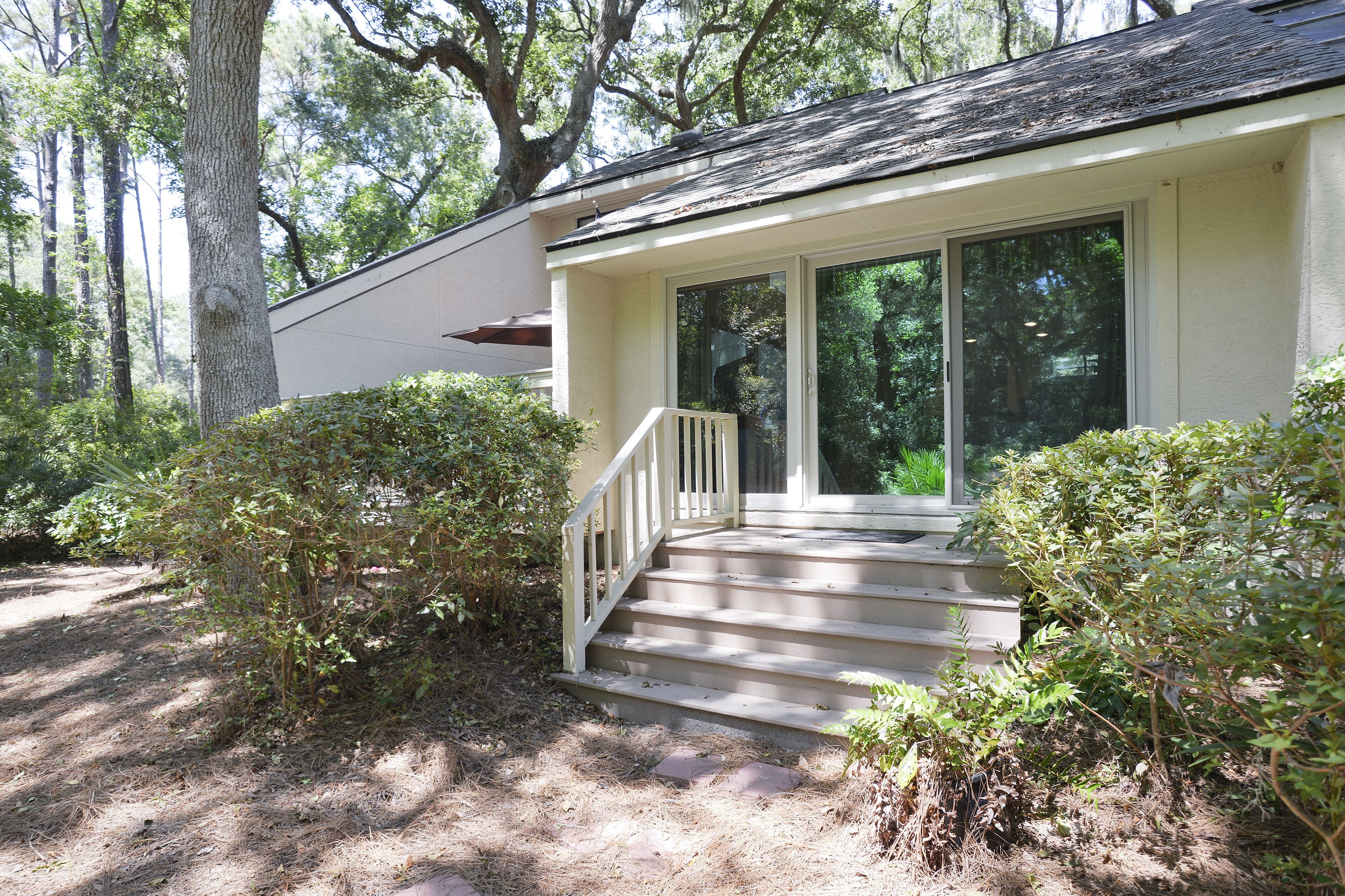 A house with a porch, a staircase leading to a door, and a surrounding wooded area.