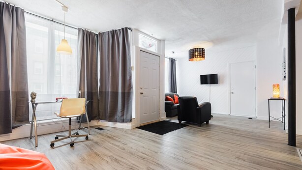 A modern living room with a wooden floor, a black sofa, a small table with a lamp, and a TV mounted on the wall.
