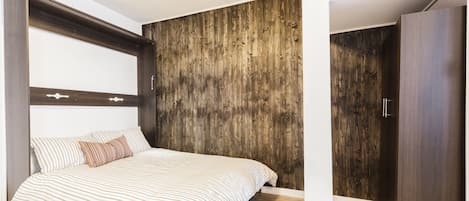 A bedroom with a bed, wooden panel wall, wardrobe, and a vent on the floor.