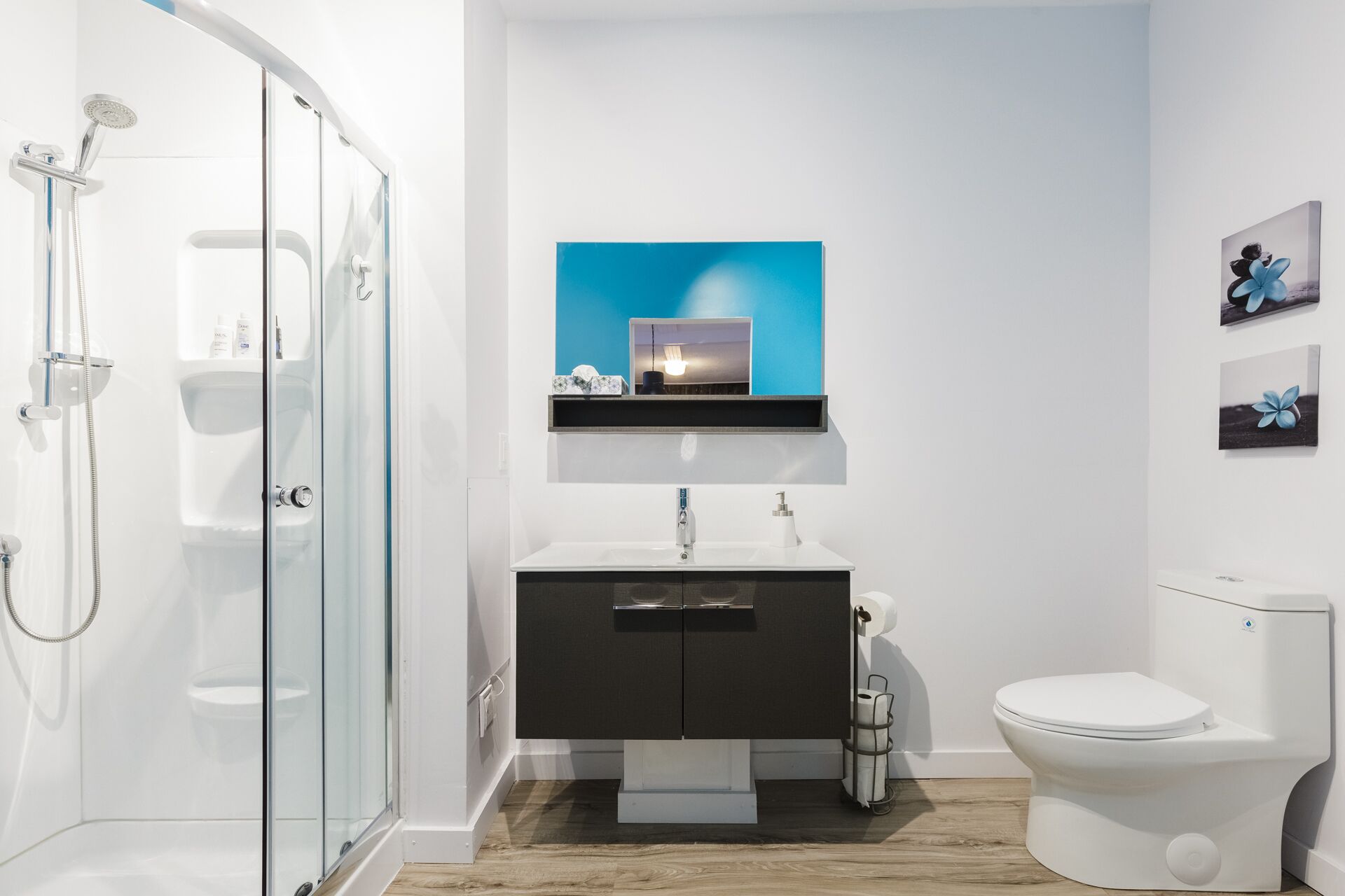 Un baño moderno con mampara de vidrio, lavamanos blanco, tocador negro y retrete.