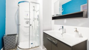 A modern bathroom with a glass-enclosed shower, a white sink with a mirror above, and a dark-toned cabinet below.