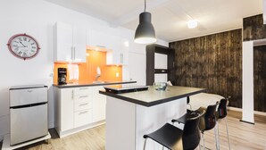 A modern kitchen with white cabinets, a black refrigerator, and a wooden accent wall.