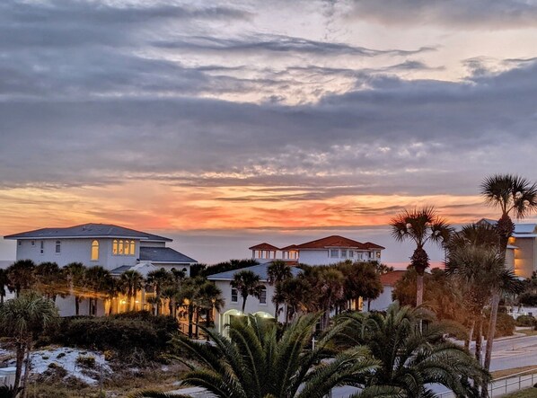 A residential area with houses and palm trees under a sunset sky.
