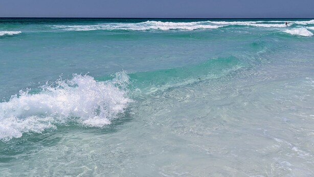 A beach with clear turquoise water and waves.