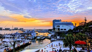 A marina with boats docked, a building with a modern design, and a sunset in the background.