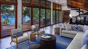 A spacious living area with a sofa, armchairs, and a coffee table, large windows offering a view of the outdoors, and a wooden staircase. - Casa Las Hijas,Private Punta Sayulita, Gated Beach Club, 5 min to town, beach (Sayulita)