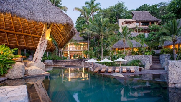 A resort pool with thatched-roof structures, stone seating, and lush greenery. - Casa Las Hijas,Private Punta Sayulita, Gated Beach Club, 5 min to town, beach (Sayulita)