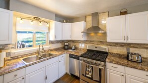A modern kitchen with white cabinets, granite countertops, stainless steel appliances, and a large window overlooking a scenic view. - Magic Escape (Oakhurst CA 93644)