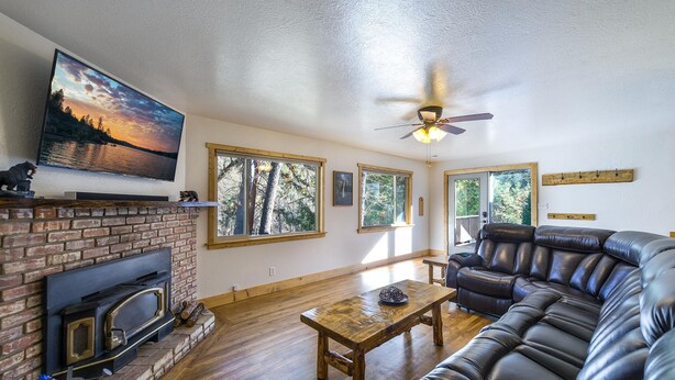 A living room with a fireplace, a large flat-screen TV, a leather sofa, and a wooden coffee table. - Magic Escape (Oakhurst CA 93644)