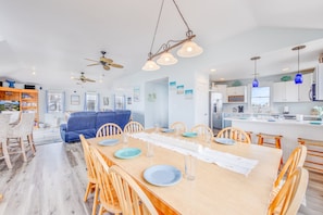 A spacious living area with a dining table set for four, a blue sofa, and a kitchen area with white cabinets and a blue pendant light.