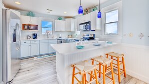 Une cuisine moderne avec des meubles blancs, un îlot central et des suspensions bleues.
