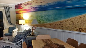 Une pièce décorée d’une fresque représentant une plage, avec une table à manger et un canapé.