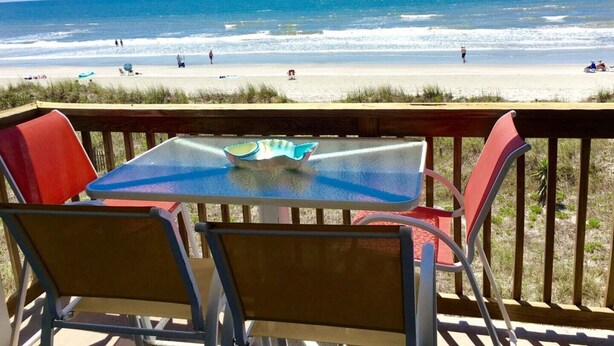 Une vue sur la plage avec une table et des chaises sur une terrasse en bois.