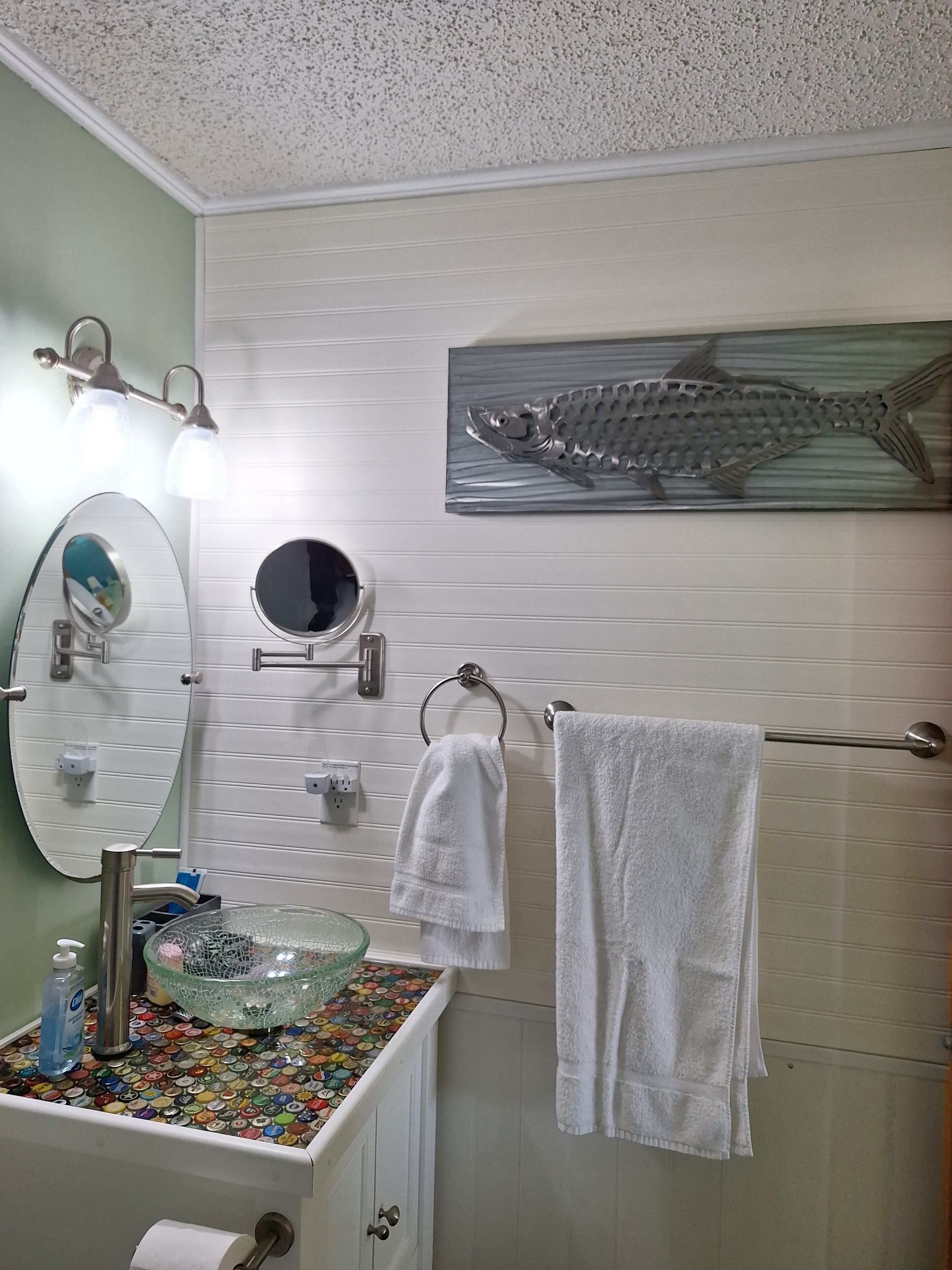Une salle de bain avec un miroir, un porte-serviettes et un motif décoratif représentant un poisson sur le mur.