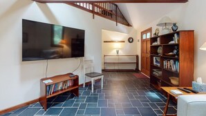 Un salon avec un téléviseur, des étagères à livres, un escalier et une lampe.