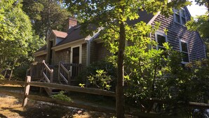 Une maison en bois rustique, dotée d’un porche et entourée d’arbres et d’une clôture en bois.
