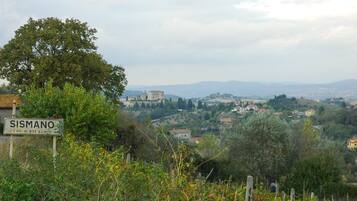 A sign indicating the location as Sismano with a view of a hilly landscape and distant buildings.