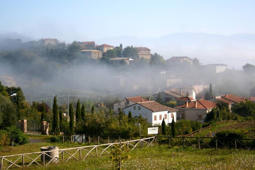 Ein Dorf mit Häusern an einem Hügelhang, umgeben von viel Grün und Bergen im Hintergrund.