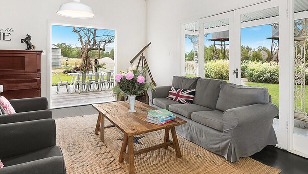 Ein modernes Wohnzimmer mit einem grauen Sofa, einem Holztisch und Blick auf einen Garten durch große Glasschwingtüren.