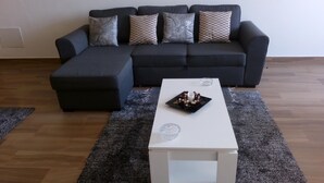 Ein Wohnzimmer mit einem dunkelgrauen Sofa, einem passenden Ottomanen und einem weißen Couchtisch mit Dekoration.