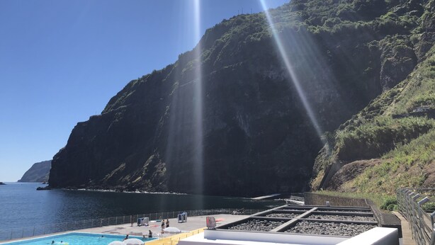 Ein Poolbereich mit Blick auf das Meer und eine gebirgige Kulisse.