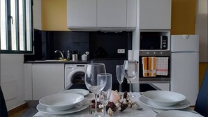 Ein Essbereich mit Tisch für vier Personen, komplett gedeckt mit Tellern, Gläsern und Besteck. Im Hintergrund sind eine Waschmaschine und eine Mikrowelle zu sehen.