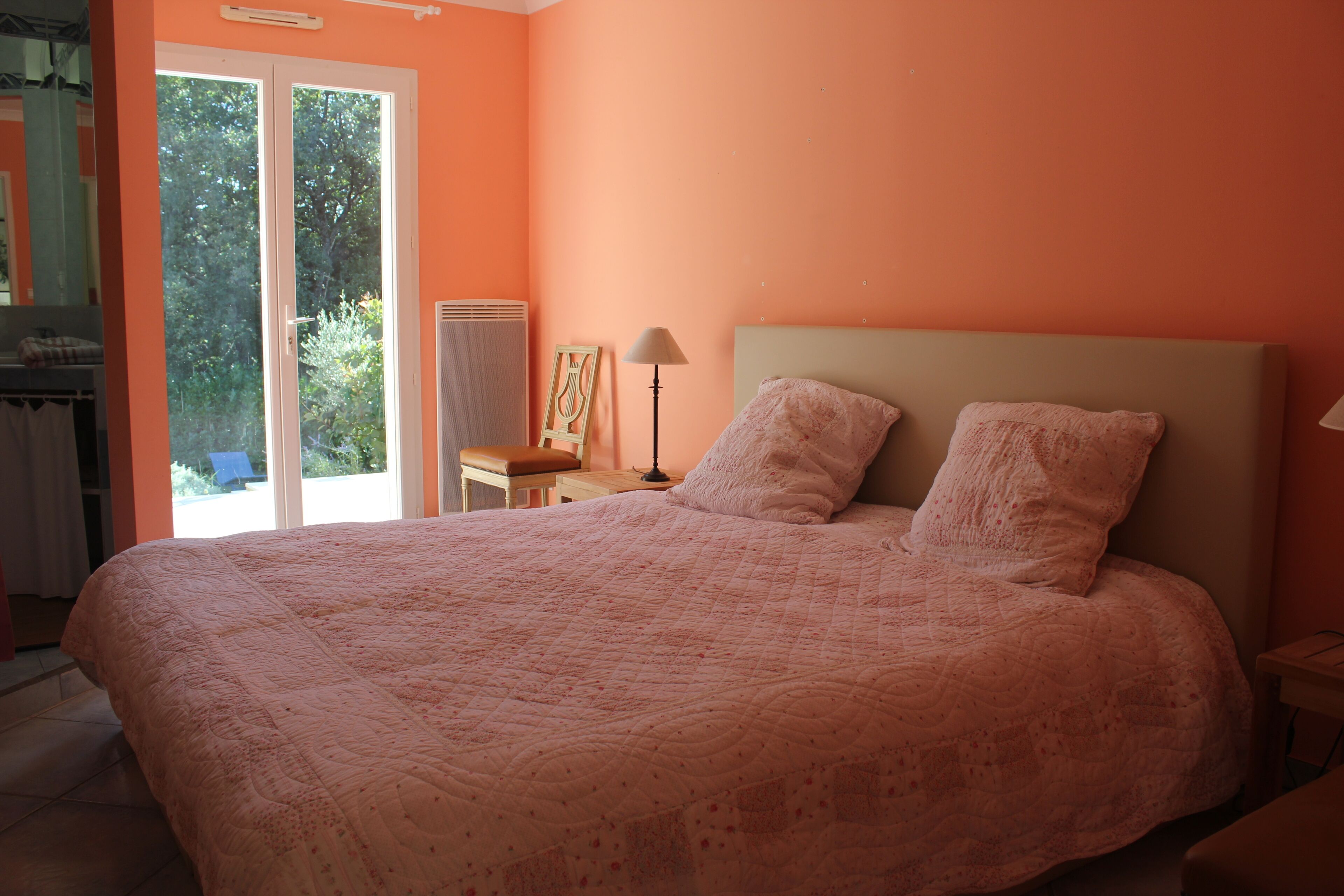 Une chambre à coucher avec un grand lit, une table de chevet, une lampe et une vue sur l’extérieur grâce à une porte coulissante.