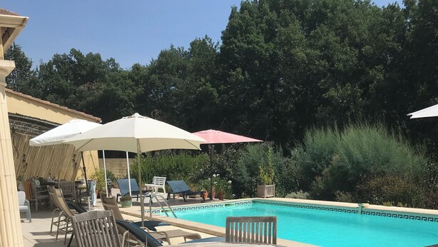 An outdoor pool area with lounge chairs and umbrellas, surrounded by greenery and a tiled patio. - Comfortable villa, heated pool in a quiet area, excluding subdivision (Sainte-Anastasie)