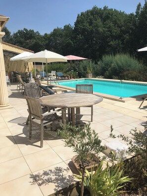 An outdoor pool area with lounge chairs and umbrellas, surrounded by greenery and a tiled patio. - Comfortable villa, heated pool in a quiet area, excluding subdivision (Sainte-Anastasie)