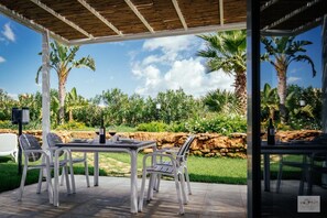 Een terras buiten met een tafel en stoelen, omringd door een stenen muur en palmbomen.