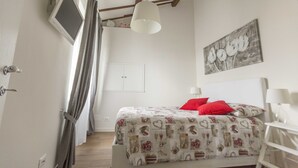 A bedroom with a bed, a painting, a ceiling fan, and a TV on the wall.