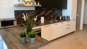 Een moderne keuken met een ingebouwde magnetron, een roestvrijstalen spoelbak en witte kasten. Op het aanrecht staan potplanten en er is een marmeren achterwand.