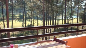 Mesa de madeira com cadeiras numa varanda com vista para uma área arborizada.