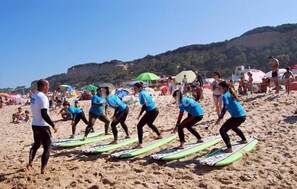 A group of people on a beach with surfboards, a person in a white shirt, and others in blue shirts. - Amazing View - Beach - Golf Resort (Herdade da Aroeira)