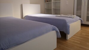 Quarto com duas camas, um guarda-roupa e uma estante com livros.