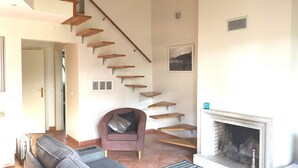 Uma sala de estar com escada, lareira, sofá e poltrona.