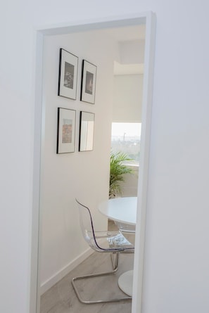 Une pièce moderne avec un mur blanc, une table ronde et une chaise transparente. Quatre tableaux encadrés sont accrochés au mur.