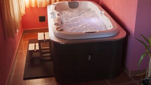 A hot tub in a room with a red wall, a small wooden stool, and a potted plant. - Spa in the house and an unbeatable view of Gredos. (San Juan de Gredos)