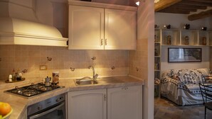 A kitchen with a gas stove, sink, and white cabinets. There is a shelf with decorative items and a framed picture on the wall. - La Casina di Pia in Alta Maremma (Montieri)