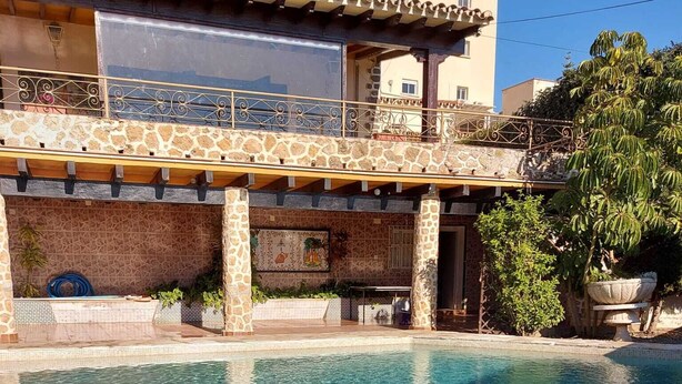 A swimming pool with stone tiles, a covered patio area, and a building with a tiled roof and stone walls. - Villa with private pool in Torremolinos  (Torremolinos)