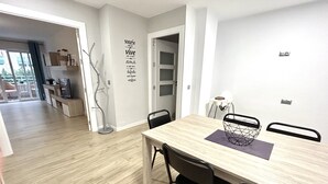 Een eethoek met een houten tafel, zwarte stoelen en een witte muur met een decoratieve spreuk.