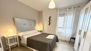 Een keurig opgemaakt slaapkamer met een bed, bedlampen, een nachtkastje, een garderobe en een raam met gordijnen.