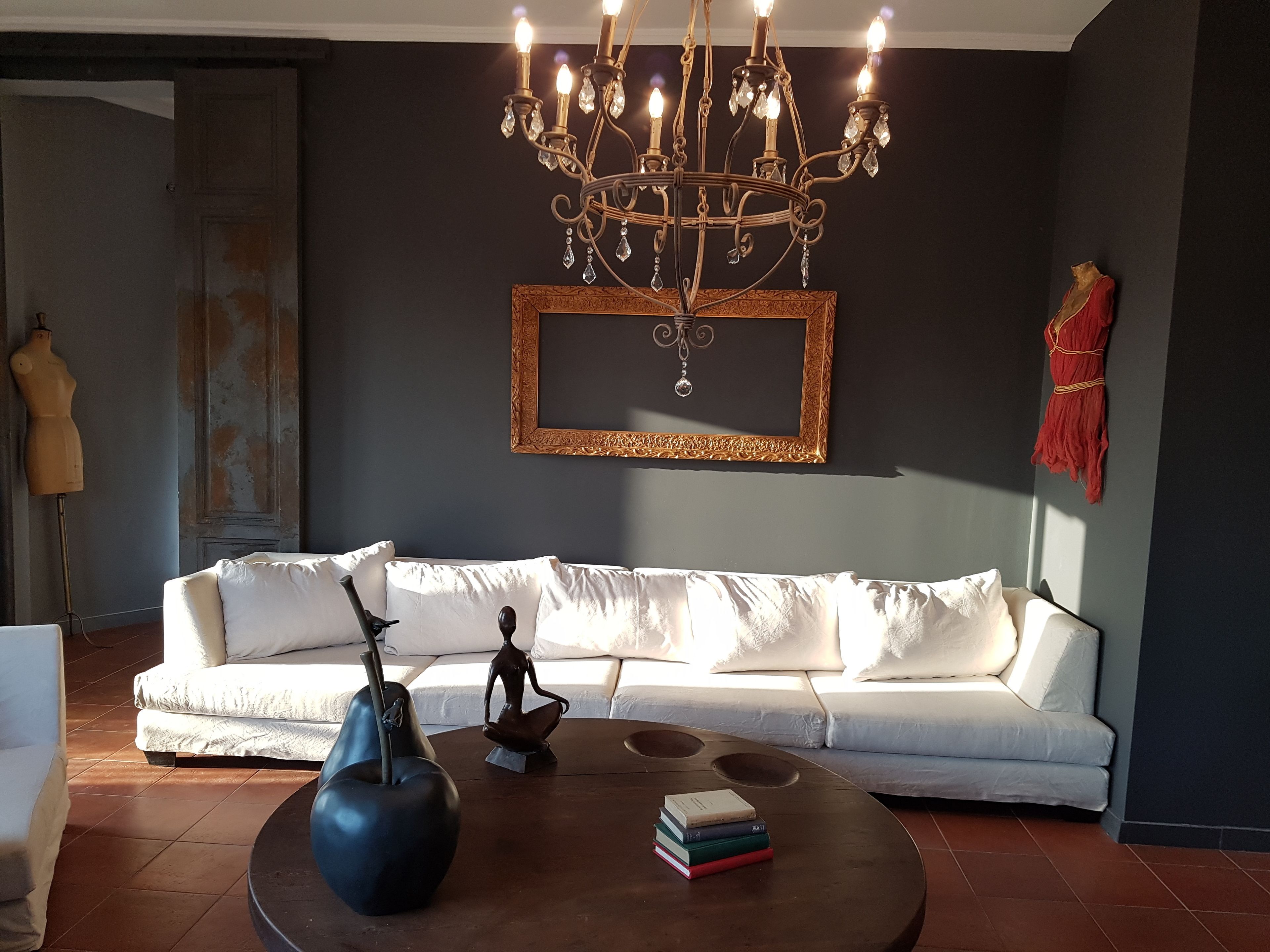 A modern living room with a white sofa, a round coffee table with books, a blue vase, and a chandelier.