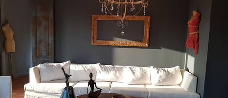 A modern living room with a white sofa, a round coffee table with books, a blue vase, and a chandelier.