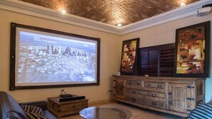 A living room with a large screen, comfortable seating, and a rustic wooden cabinet. - Beautiful house in San Carlos (SAN CARLOS)